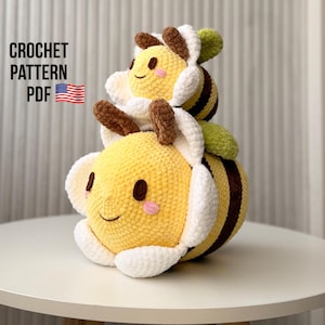 Può includere: Due peluche a forma di ape all'uncinetto, uno impilato sull'altro. Le api sono gialle con dettagli marroni e bianchi e hanno facce sorridenti. Il testo "CROCHET PATTERN PDF" è visibile nell'immagine.