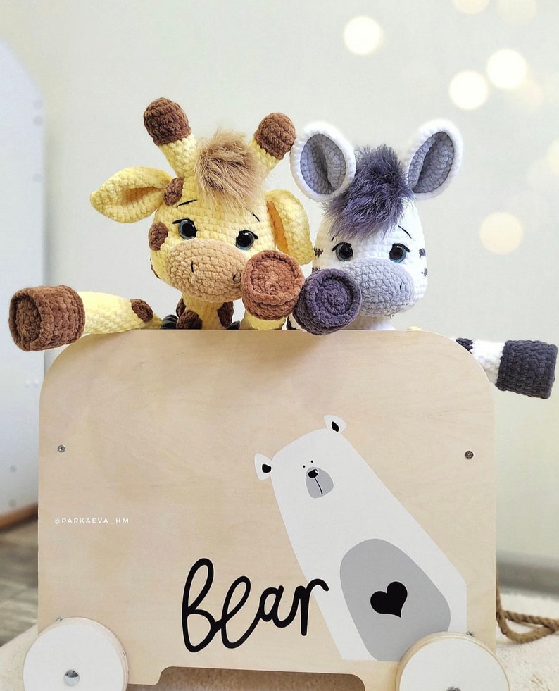 May include: A wooden toy wagon with a white polar bear illustration and the word "bear" printed on the side. Two crocheted stuffed animals, a giraffe and a zebra, are sitting in the wagon.