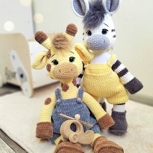 May include: A crocheted yellow giraffe with blue overalls and a brown toy airplane, standing next to a crocheted zebra with yellow overalls and black and white stripes.