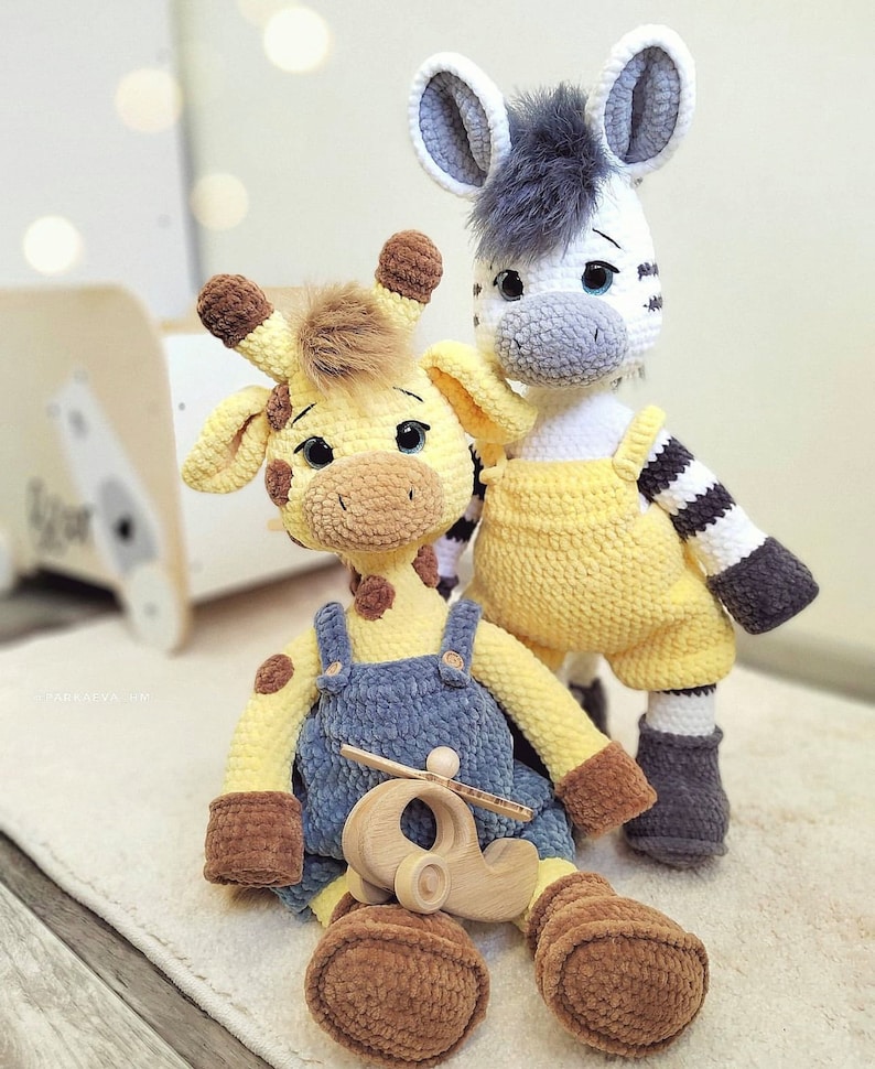 May include: A crocheted yellow giraffe with blue overalls and a brown toy airplane, standing next to a crocheted zebra with yellow overalls and black and white stripes.