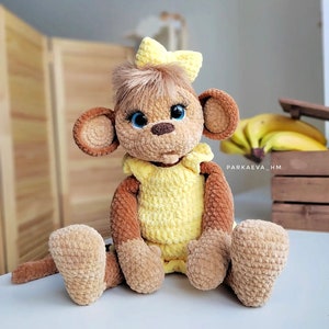 May include: A crocheted monkey toy wearing a yellow dress and a yellow bow. The monkey has brown fur, blue eyes, and a brown nose.