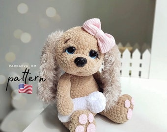 May include: A handmade crochet bunny doll in shades of tan and beige, with a pink bow and blue eyes. The bunny is holding a white bone and has pink paw pads. The word "pattern" is visible in the image.