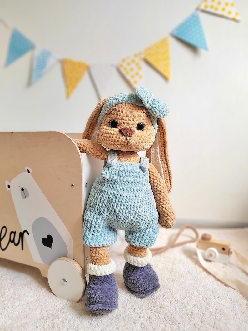 May include: A crocheted bunny toy wearing blue overalls and a blue headband with a bow. The bunny is standing next to a wooden toy box with a white polar bear illustration and the word "bear" on the side.