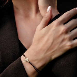 Può includere: Un braccialetto in corda nera con un ciondolo a forma di ape dorata. L'ape è decorata con disegni intricati.