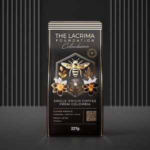 Puede incluir: Una bolsa de café negra con detalles dorados que presenta una abeja y un diseño floral. La bolsa está etiquetada como "The Lacrima Foundation Colombiana" e incluye un código QR. La bolsa contiene 227 gramos de café de origen único de Colombia.