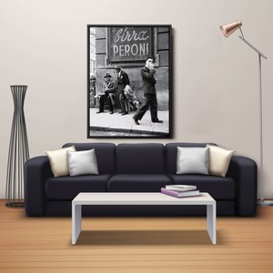 May include: A black and white framed print of a vintage street scene with the text "birra PERONI". The print hangs above a black sofa with white pillows and a white coffee table. A modern floor lamp and decorative black metal sculpture are also in the room.