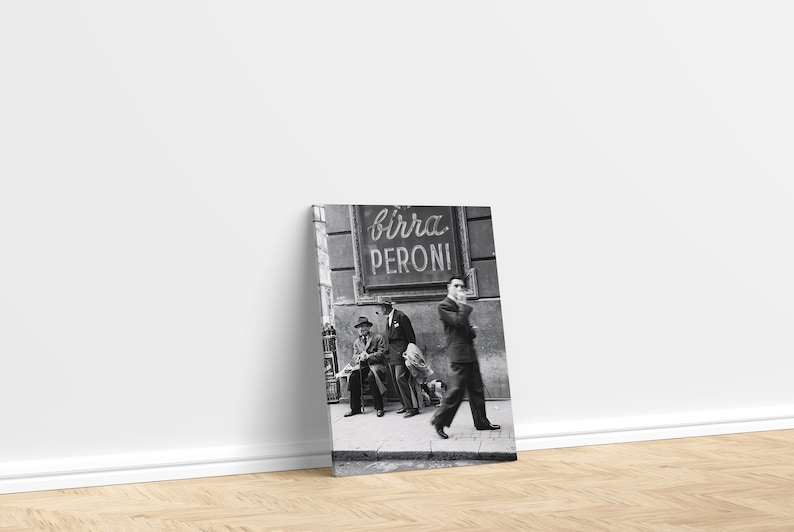 May include: Black and white photograph of a street scene with three men in suits and hats, one walking and two seated. A sign for "Birra Peroni" is visible above them. The image is displayed on a canvas print.