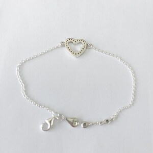 Puede incluir: Pulsera de plata con un dije en forma de coraz&oacute;n. El dije tiene un dise&ntilde;o punteado dentro de la forma del coraz&oacute;n. La pulsera tiene una cadena delicada y un cierre de broche. Presentada sobre un fondo blanco.
