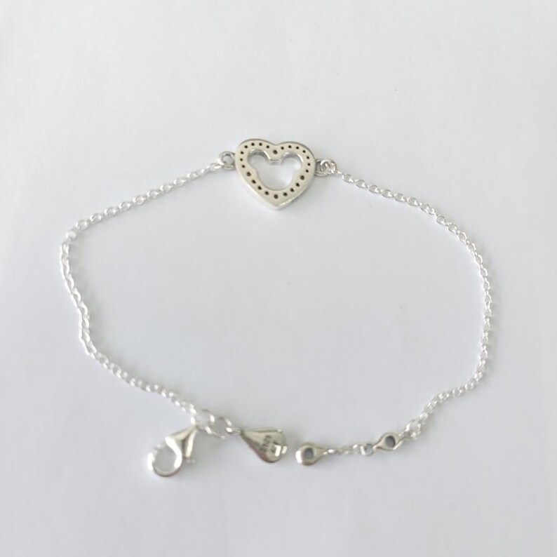 Puede incluir: Pulsera de plata con un dije en forma de coraz&oacute;n. El dije tiene un dise&ntilde;o punteado dentro de la forma del coraz&oacute;n. La pulsera tiene una cadena delicada y un cierre de broche. Presentada sobre un fondo blanco.