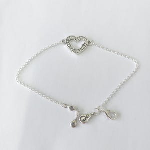 Puede incluir: Una pulsera plateada con un dije en forma de coraz&oacute;n con la silueta de Mickey Mouse. El dije est&aacute; incrustado con peque&ntilde;as piedras transparentes. La pulsera tiene una cadena delicada y un cierre de mosquet&oacute;n.