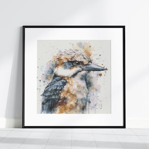 Op de afbeelding: Een aquarel schilderij van een kookaburra met blauwe en bruine veren. De vogel kijkt naar links en heeft een lichtblauwe achtergrond met aquarel spatten.