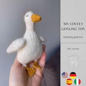 Op de afbeelding: Een handgebreid wit gansje speelgoed met een gele snavel en gele zwemvliezen. De tekst luidt MY LOVELY GOSLING TOY knitting pattern, flat version, vergezeld van een lijntekening van een gebreid vierkant en vier vlagpictogrammen.
