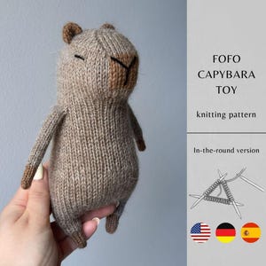 Puede incluir: Un juguete de carpincho tejido en tonos marrones, con la cara y las orejas de color marrón oscuro. El juguete se sostiene en una mano. El texto de la derecha dice "FOFO CAPYBARA TOY knitting pattern".