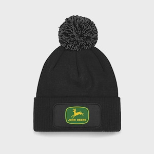 May include: Black knitted beanie hat with a large pom-pom. The front has a rectangular patch displaying the John Deere logo: a leaping deer in yellow and green, with the words "JOHN DEERE" below.
