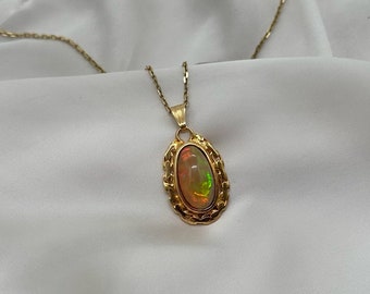 May include: A gold chain necklace with a pendant featuring a large oval opal gemstone set in a gold frame.