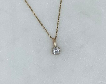May include: A delicate gold chain necklace with a small, clear round pendant.