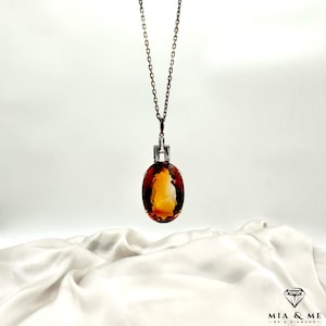 May include: A gold chain necklace with a large oval-shaped orange gemstone pendant. The pendant is set in a silver bezel with small diamonds around the edge.