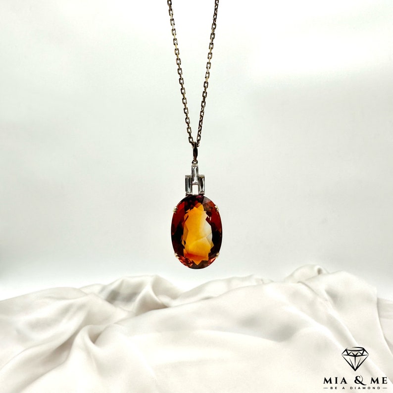 May include: A gold chain necklace with a large oval-shaped orange gemstone pendant. The pendant is set in a silver bezel with small diamonds around the edge.