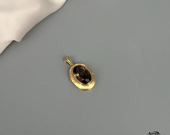 May include: A gold pendant with an oval, smoky quartz gemstone. The pendant has a simple, elegant design with a gold bail. The gemstone is a rich, dark brown color, set in a gold bezel.