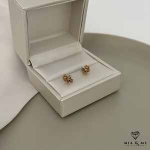 K&ouml;nnte beinhalten: Ein Paar goldene und silberne Ohrringe in Blumenform in einer wei&szlig;en Schachtel. Die Ohrringe sind klein und zart.