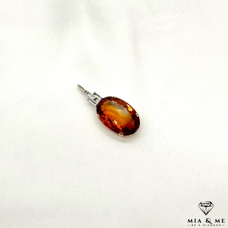 May include: A gold pendant featuring a large, oval-shaped, orange gemstone set in a silver bezel.