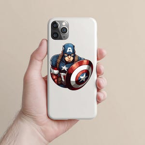 以下が含まれることがあります： キャプテン・アメリカのグラフィックが描かれた白い携帯電話ケース。イラストは、キャプテン・アメリカが青、赤、白の象徴的なコスチュームを着て、シールドを持っている様子を描いています。シールドは、中央に星がある赤と白の円形デザインです。