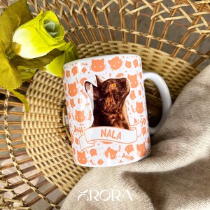 May include: A white ceramic mug with a cat print and the name "Nala" on it. The mug has a handle and is filled with a brown cat.