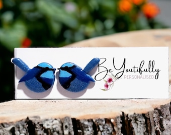 May include: A pair of bluebird earrings, made of polymer clay, with a blue and black design. The earrings are on a white card with the text "Be Youtifully Personalised".