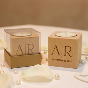 May include: Two wooden candle holders with engraved initials "AR" and a date. One is in a clear box. The scene includes white flower petals, pearls, and heart-shaped decorations, suggesting a wedding theme.