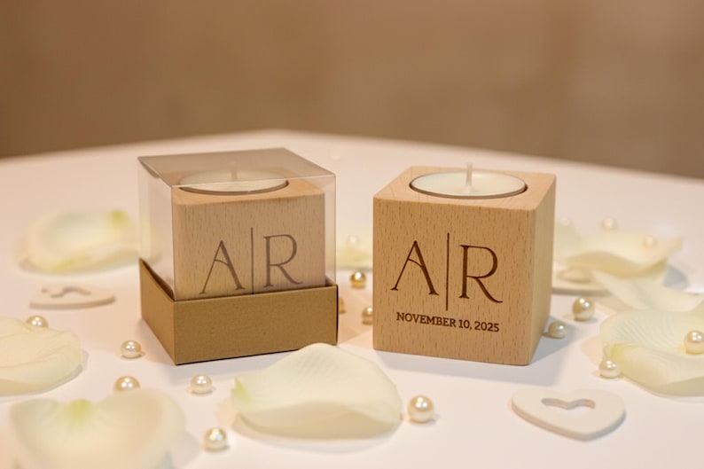 May include: Two wooden candle holders with engraved initials "AR" and a date. One is in a clear box. The scene includes white flower petals, pearls, and heart-shaped decorations, suggesting a wedding theme.