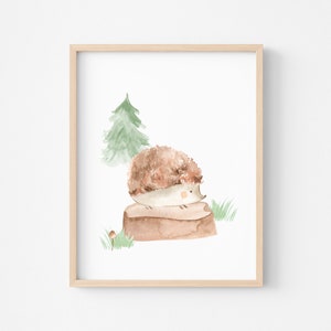 May include: Watercolor illustration of a hedgehog sitting on a tree stump, with a green tree and grass in the background. The artwork is framed in a light wood frame. The hedgehog is brown and white, and the overall theme is nature.