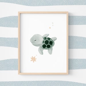 Può includere: Una stampa ad acquerello incorniciata con una tartaruga marina sorridente con un guscio verde e verde scuro. L'opera d'arte ha una cornice in legno chiaro ed è ambientata su uno sfondo bianco con un motivo a strisce blu e bianche.