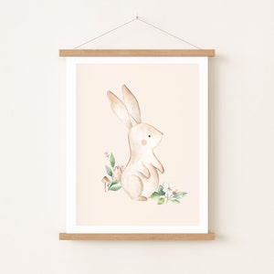 May include: A watercolor illustration of a brown bunny rabbit standing on a peach background with green leaves and pink flowers.