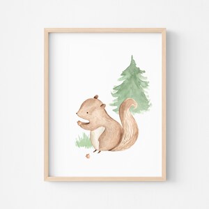 May include: Watercolor illustration of a brown squirrel holding a nut, set against a green pine tree and grass. The artwork is framed in a light wood frame, perfect for nursery or children's room decor.