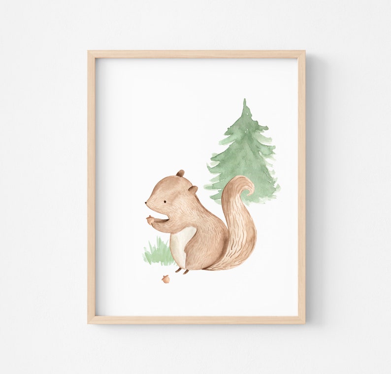 May include: Watercolor illustration of a brown squirrel holding a nut, set against a green pine tree and grass. The artwork is framed in a light wood frame, perfect for nursery or children's room decor.