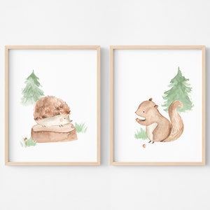 May include: Two framed watercolor prints featuring woodland animals. One print shows a hedgehog on a log, the other a squirrel with a nut. Both have a green tree and grass on a white background, framed in light wood.