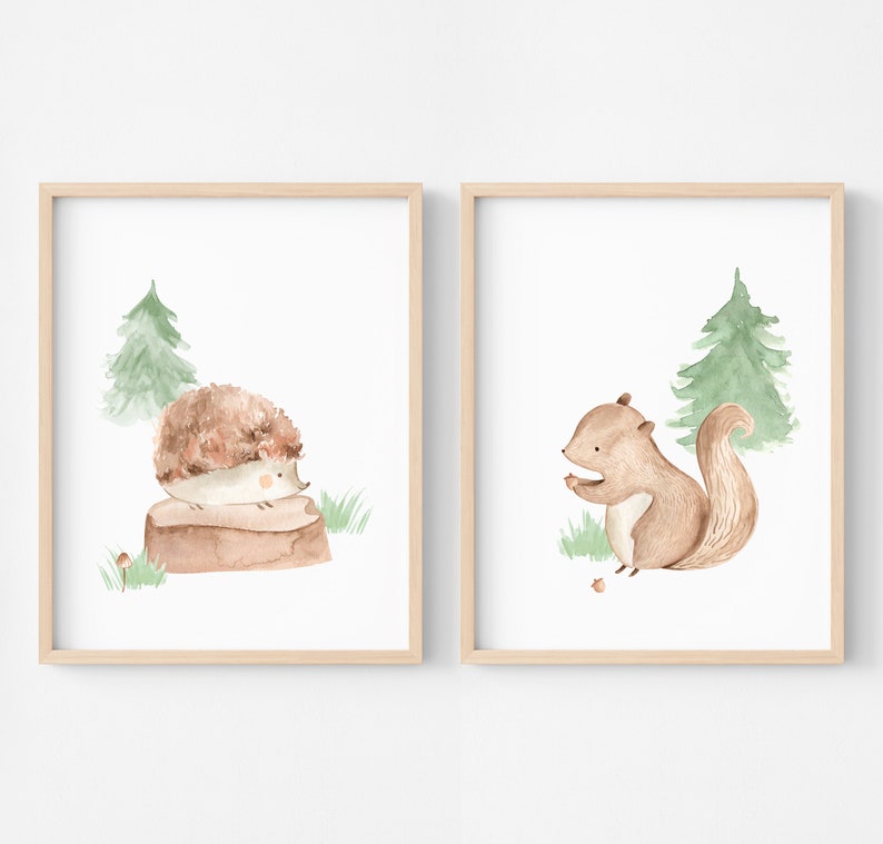May include: Two framed watercolor prints featuring woodland animals. One print shows a hedgehog on a log, the other a squirrel with a nut. Both have a green tree and grass on a white background, framed in light wood.