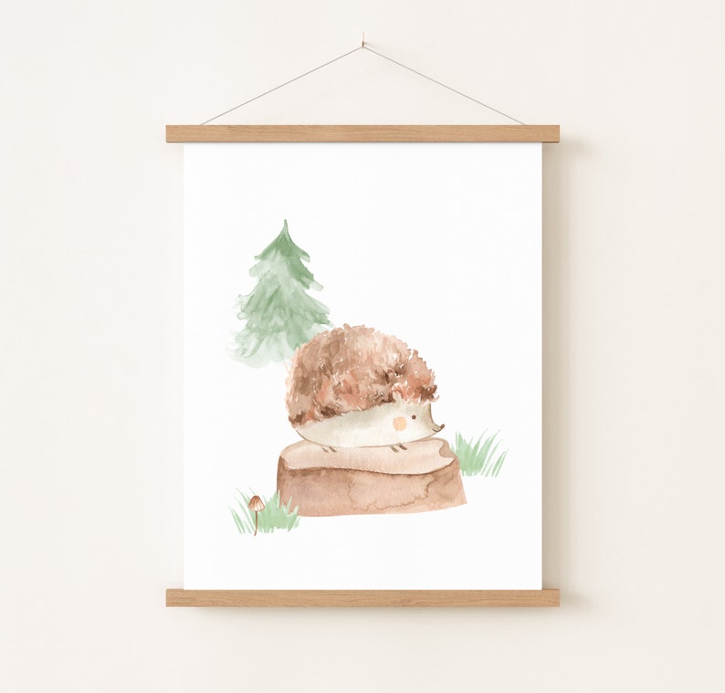 May include: Watercolor print of a hedgehog sitting on a log, with a green tree and grass in the background. The hedgehog has brown and beige fur. The artwork is displayed on a white background and framed with a wooden hanger.