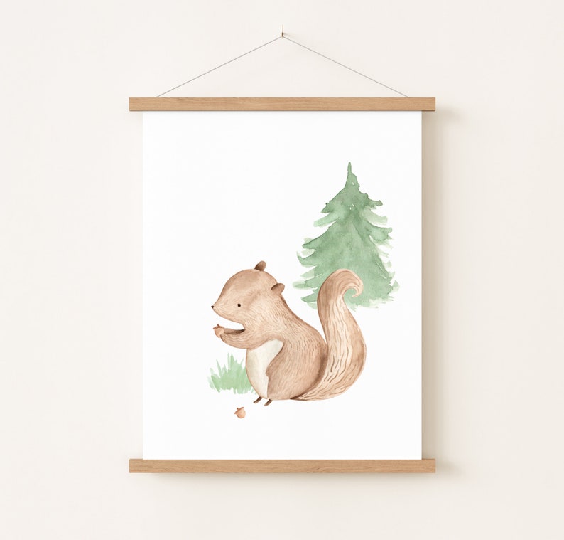 May include: Watercolor print of a brown squirrel holding a nut, with a green pine tree in the background. The artwork is displayed on a white background and framed with a wooden magnetic poster hanger. The style is whimsical and suitable for a nursery.