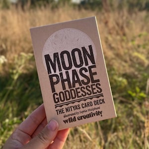 May include: A rectangular card deck box made of light brown kraft paper. The front features a circular graphic and bold black text that reads: MOON PHASE GODDESSES, THE NITYAS CARD DECK, illustrated by Sophie Maliphant, and wild creativity.