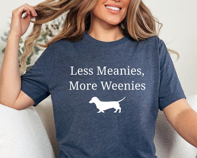 May include: A navy blue t-shirt with the text "Less Meanies, More Weenies" and a white silhouette of a dachshund. The shirt is made of a soft material.