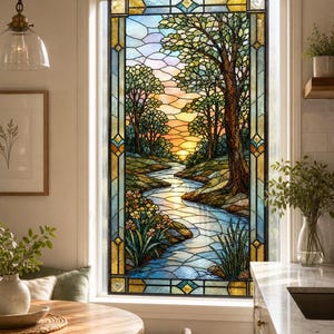 Puede incluir: Un panel de ventana de vidriera rectangular que presenta un paisaje de un río serpenteante que fluye a través de un bosque al atardecer. El diseño incluye árboles, orillas cubiertas de hierba y flores en tonos verdes, naranjas, amarillos y azules.