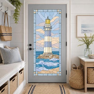 May include: A gray door featuring a large stained glass window panel depicting a lighthouse with blue and white stripes, standing on a rocky base amidst blue ocean waves, set against a pale blue sky with soft peach-colored clouds.