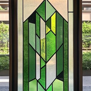 Puede incluir: Una ventana de vidrio emplomado con un diseño geométrico que presenta piezas de vidrio verde, amarillo y blanco.
