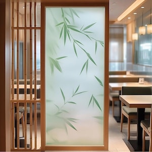 Puede incluir: Un film de ventana de vidrio esmerilado con un diseño de hojas de bambú verdes sobre un fondo blanco. El film está instalado en una habitación con paredes de madera y una vista de un comedor con mesas y sillas.