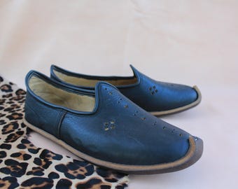 Può includere: Un paio di scarpe da uomo in pelle blu scuro senza lacci con un design traforato. Le scarpe hanno una punta arrotondata e un tacco leggermente appuntito.