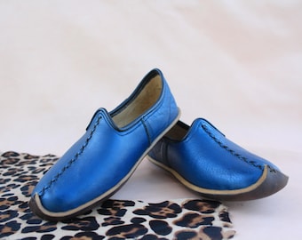 Può includere: Un paio di scarpe blu in pelle da indossare senza lacci con punta a punta e design cucito. Le scarpe sono su un tessuto con stampa leopardata.