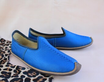 Può includere: Un paio di scarpe da uomo in pelle blu da infilare con un dettaglio cucito sulla parte superiore. Le scarpe hanno una punta arrotondata e una suola piatta.