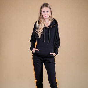 May include: Black hooded sweatshirt and matching sweatpants with yellow side stripes. The model is wearing brown ankle boots.