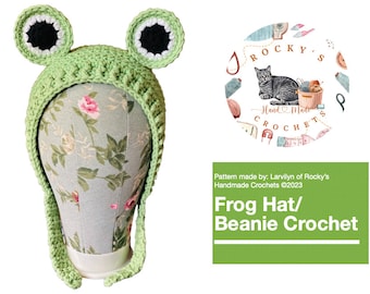 May include: Green crocheted frog hat with white and black accents. The hat is on a mannequin head with a floral pattern. The text "ROCKY'S Hand Made CROCHETS" is in a circle with a cat and yarn.